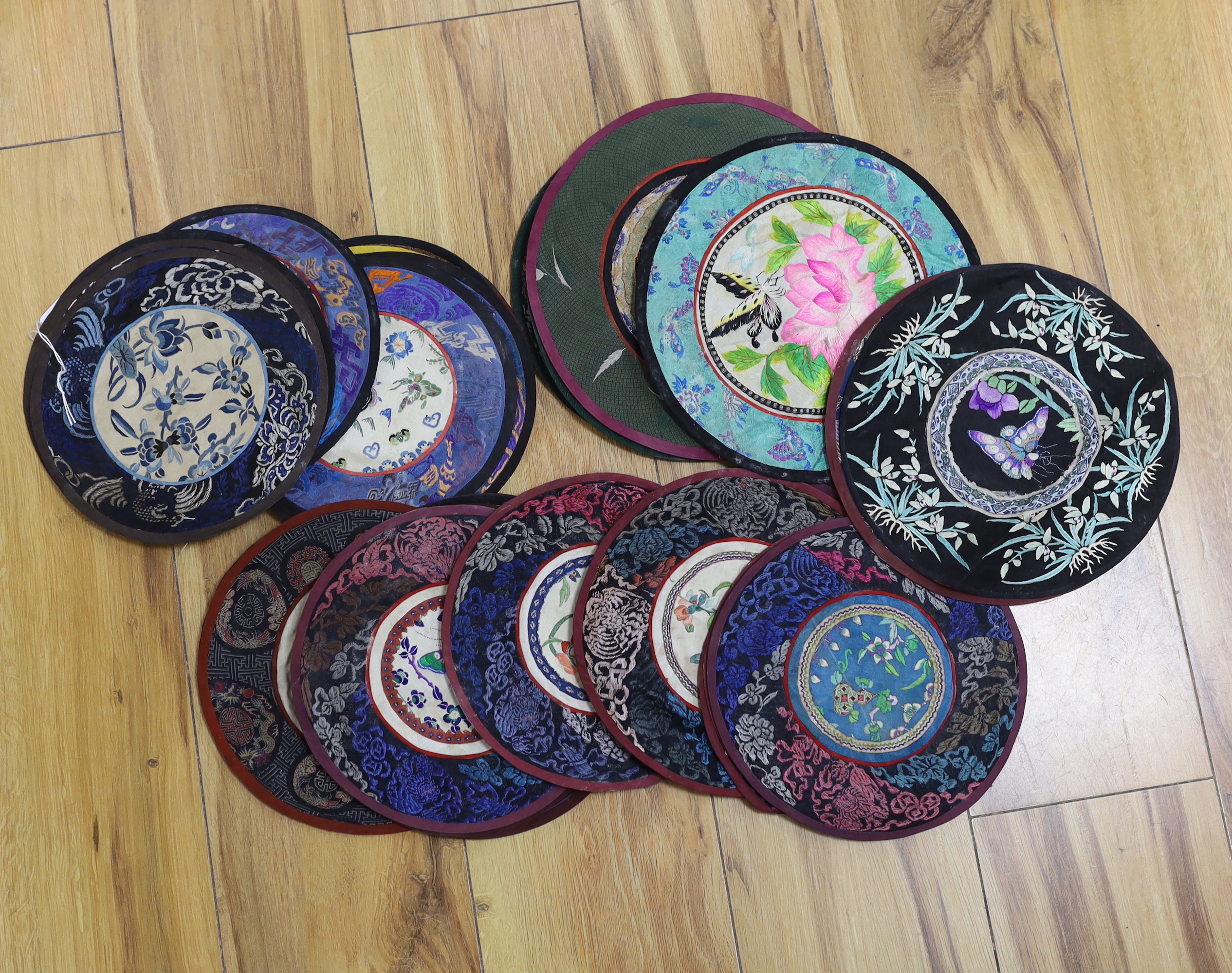 Forty two Chinese embroidered circular mats with damask borders, largest 25cm in diameter